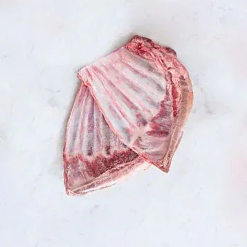 Raw lamb rib offcuts on a white marble surface, showing pink meat and bones