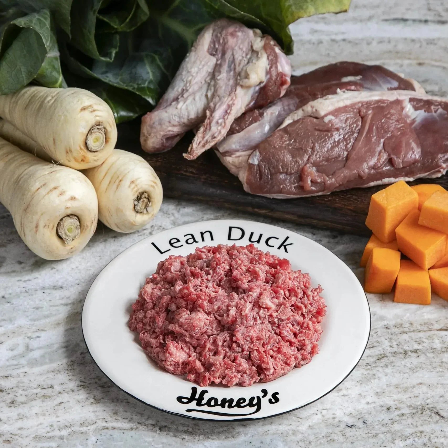 Plate of raw lean duck mince with fresh duck meat, cubed carrots, parsnips, and leafy greens