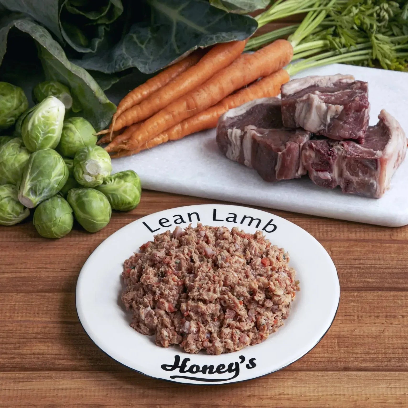 Plate of lean lamb minced meat with fresh carrots, brussels sprouts, and lamb chunks on a wooden table