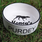 White ceramic dog bowl labeled "Purdey" with black greyhound silhouette and "Honey's" text inside, on grass