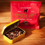 Beautiful Joe's Ethical Dog Treats red bag with open yellow tin of dog treats on wooden surface